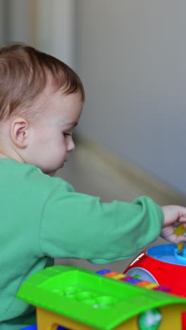 caucasian baby playing with a toy on the floor. calm kid presses on toy mouth but it pops up again. christmas tree at backdrop. vertical video