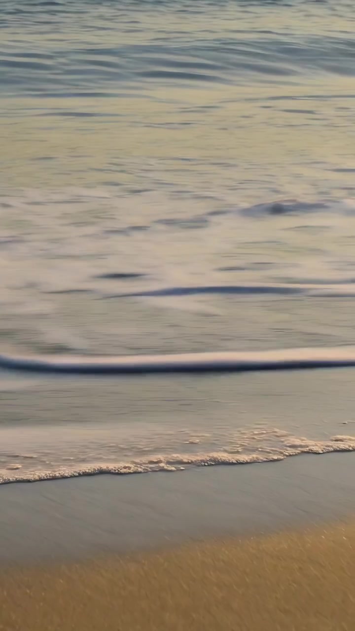 Video verticale: Onde che avanzano e si ritirano su una spiaggia sabbiosa, una piccola mareggiata che crea schiuma più ampia.