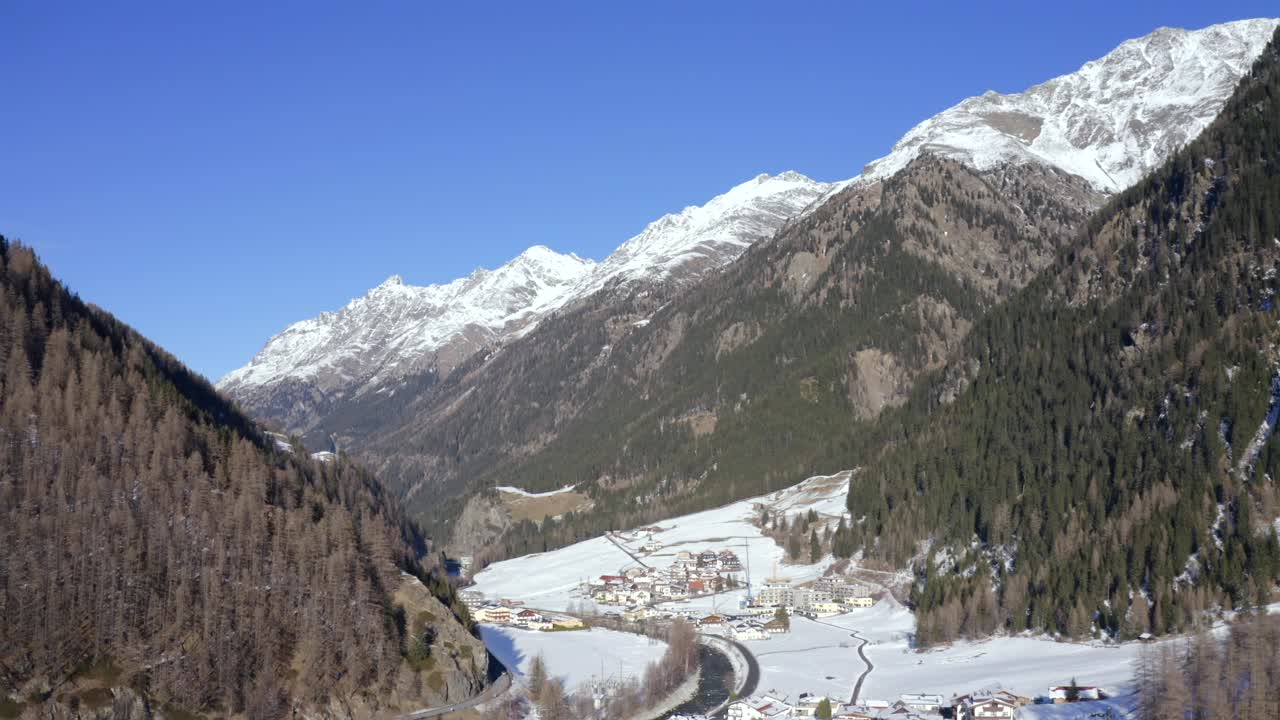 A panoramic aerial shot of Sölden village surrounded by forested and snow-covered mountains.
