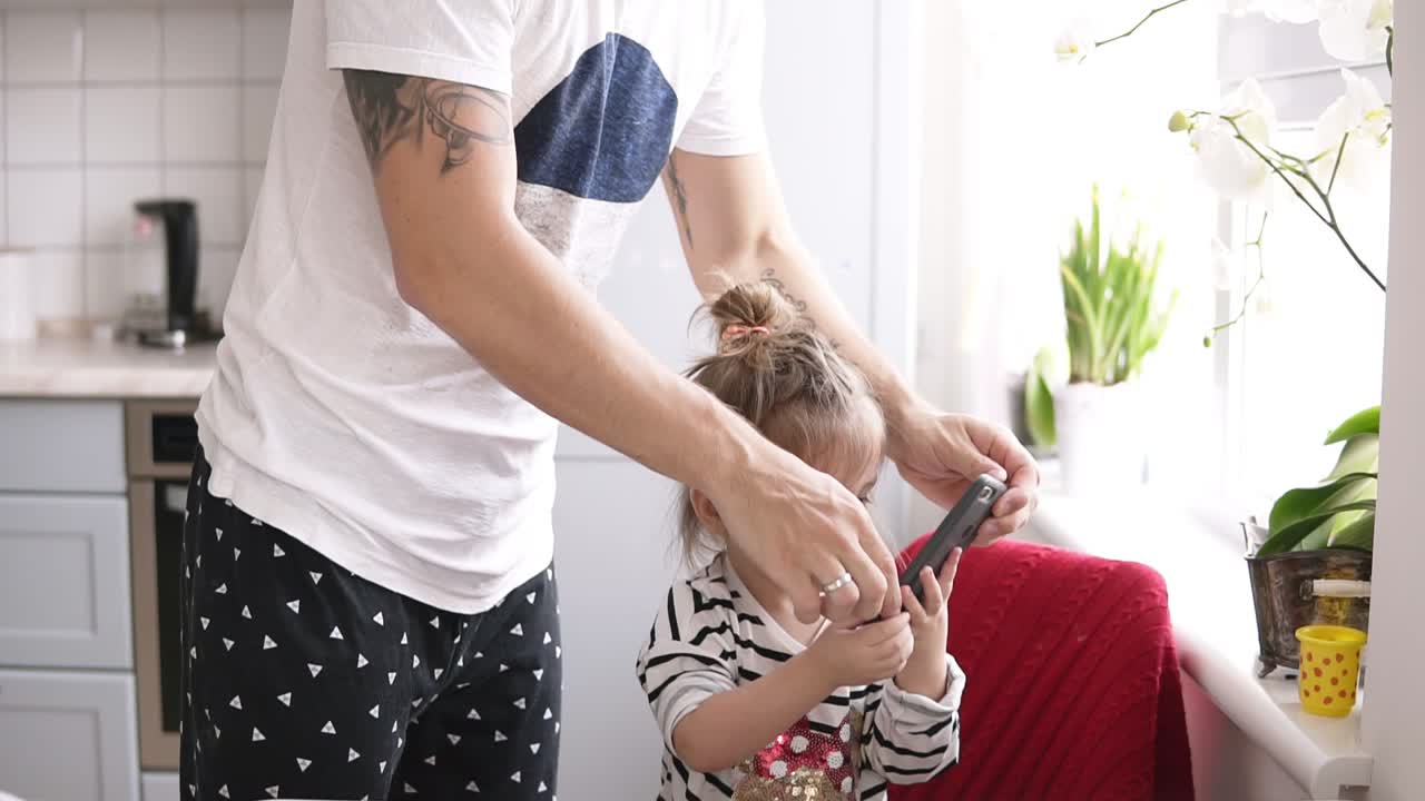 una niña linda hablando por teléfono, papá está de pie cerca en la cocina