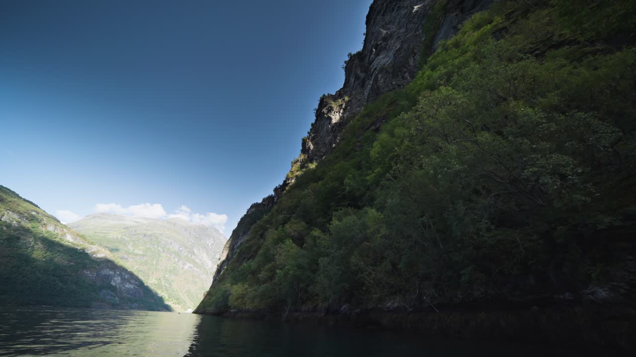 A kayaker glides through the calm waters of Geiranger Fjord, surrounded by steep cliffs and lush greenery.