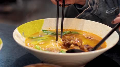 person enjoying spicy noodle soup with chopsticks