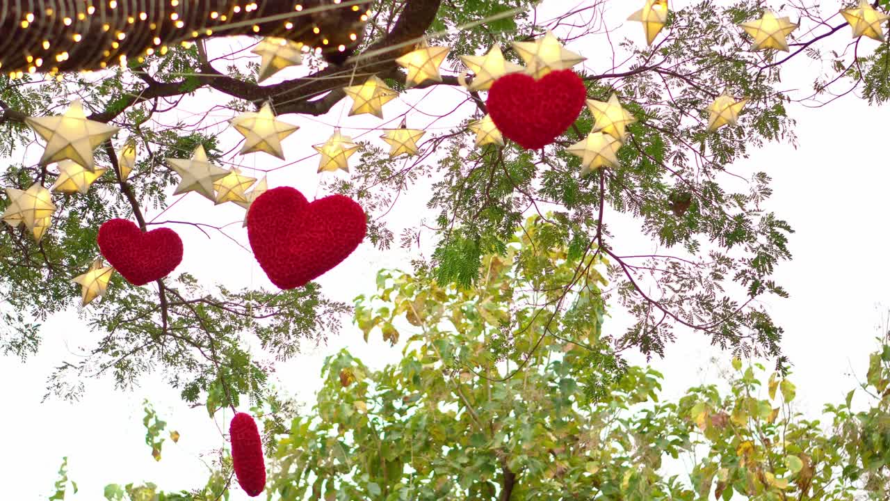 corazones rojos colgando de un árbol con muchas estrellas de papel y luces parpadeando por la noche. concepto del día de san valentín
