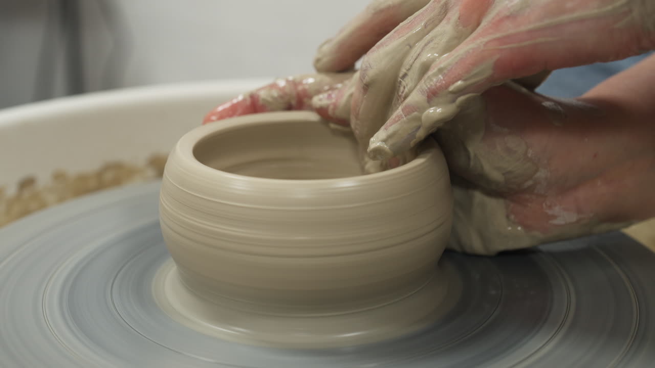 Medium shot of white hands making mug from clay, interior