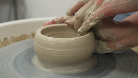 medium shot of white hands making mug from clay, interior