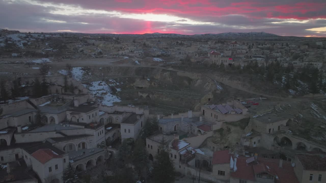 Veduta aerea del villaggio di Mustafapaşa in Cappadocia, Turchia, che mostra le storiche case rupestri in pietra e le strade tranquille sotto un drammatico cielo rosa al tramonto in inverno