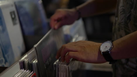 Man's-Hands-Searching-And-Choosing-Vinyl-Record-Displayed-In-The-Shelf-In-A-Music-Record-Shop