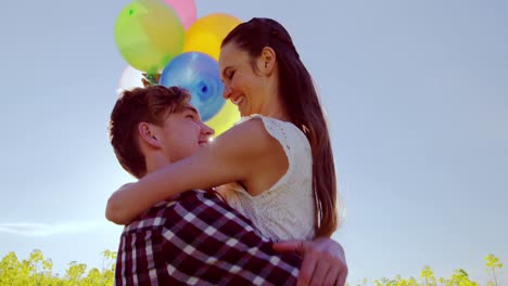 Romantic-couple-holding-colorful-balloons-and-embracing-each-other-in-mustard-field