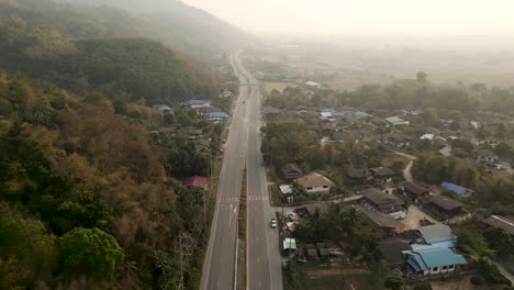 aerial view of a highway passing through a rural village with mountains and fields in hazy conditions