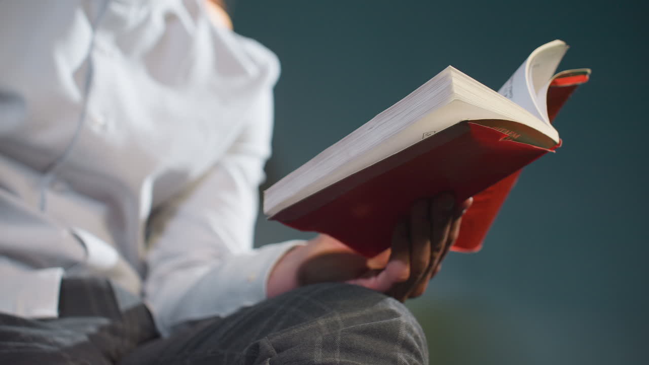 색 셔츠와 회색 바지를 입은 남성이 빨간 책과 큐 스틱을 들고 손을 무에 고 손가락으로 큐스틱을 잡고 부드러운 조명이 텍스처를 강조합니다.