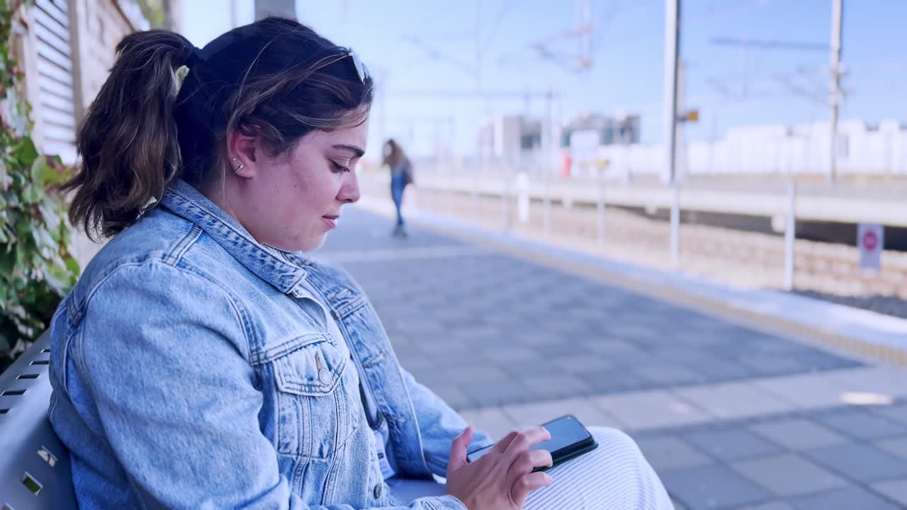 Young Woman Using Her Phone at an Outdoor Train Station