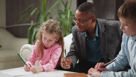 Black-man-teacher-sits-with-little-children-doing-homework