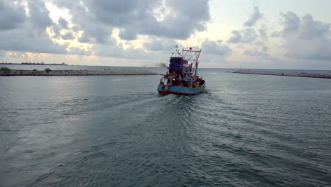 a slow following up shot from a drone of a fishinb boat cruising out of a bay into the ocean during a sunrise, thailand.