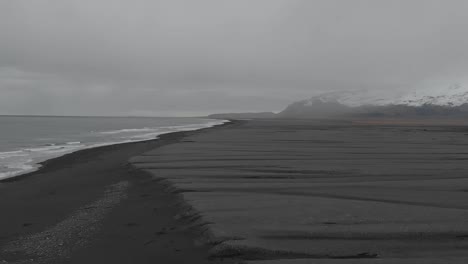 slow motion drone shot flying back along the vast black sand beach