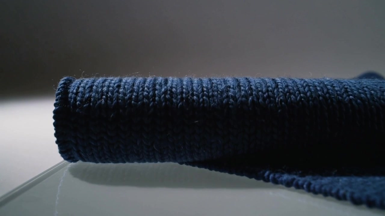 Kamera dras tillbaka och avslöjar en rullad blå handduk som rullas ut på glas, visar stickad textur och grå vägg