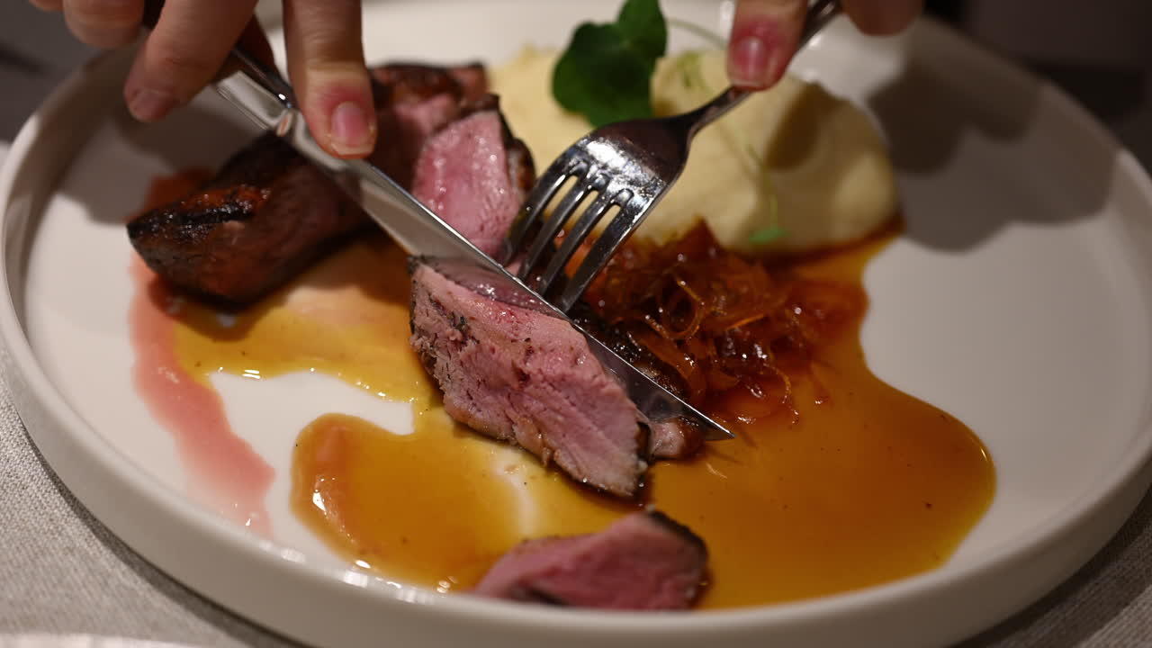 Woman cutting juicy duck breast on plate with knife and fork during fine dining meal
