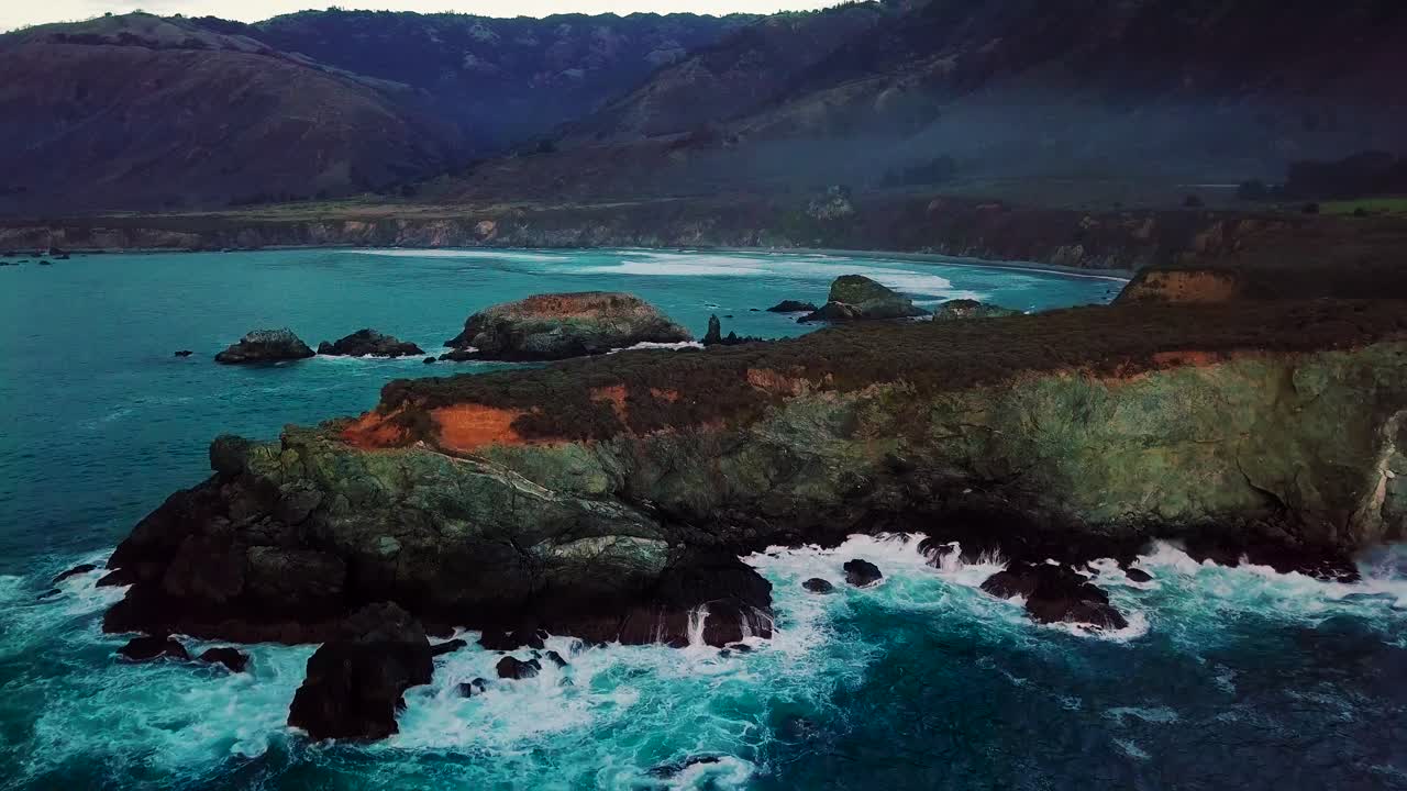 Twilight aerial wide view of waves crashing on rocky ocean cliffs at Sand Dollar Beach in Big Sur California