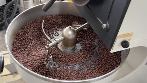 aromatic fresh specialty coffee beans spinning on cooling and mixing tray in regular speed to reduce the heat evenly after roasting, production warehouse factory shot of food and beverage industry