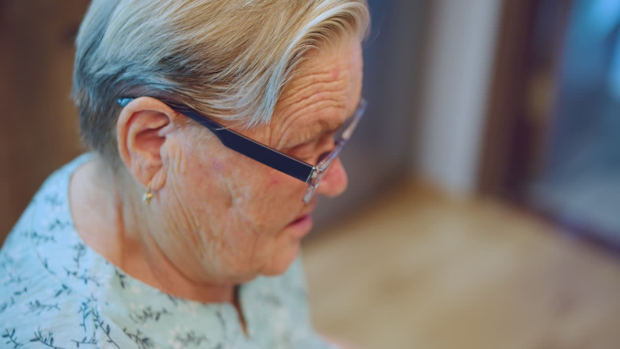 Anziana signora con occhiali che riposa a casa. Donna anziana seduta pacificamente nella sua confortevole residenza. Un'anziana signora con occhiali seduta tranquillamente nei confini accoglienti della sua casa.