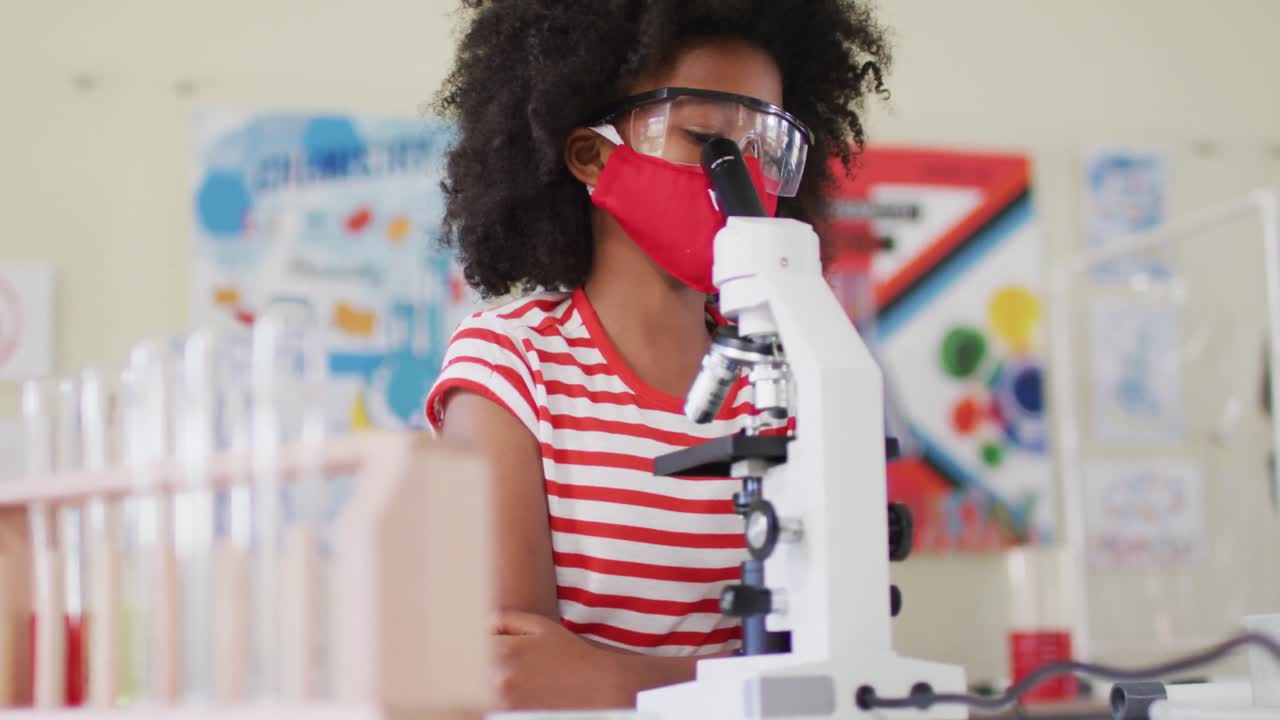niña con máscara facial y gafas protectoras usando microscopio en el laboratorio