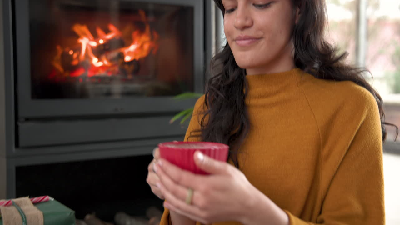 Navidad, mujer cómoda disfrutando de una bebida caliente junto a la chimenea, con una diadema festiva en casa.