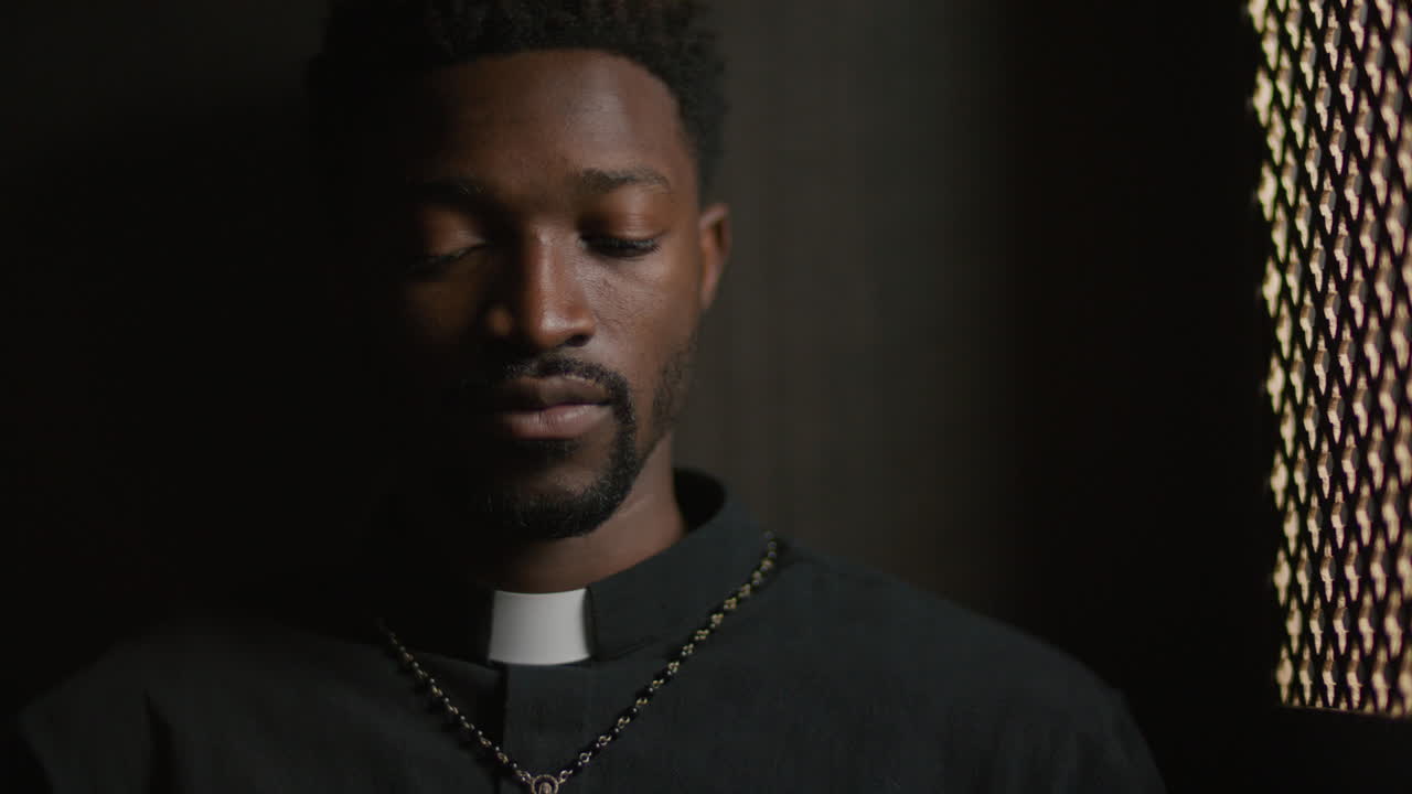 Jovem padre afro-americano lendo a Bíblia em um confessionário