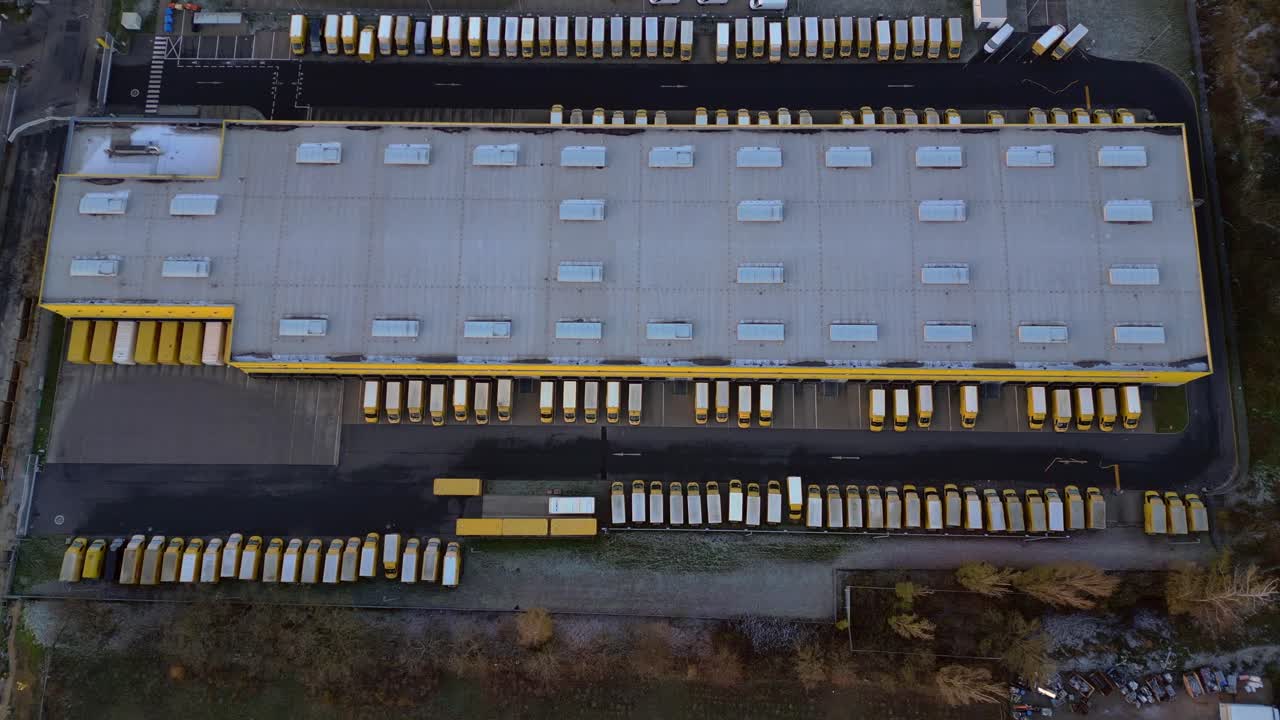 Large warehouse facility with numerous trucks parked at loading docks, representing global distribution. Spectacular aerial view overflight flyover drone top down Above view