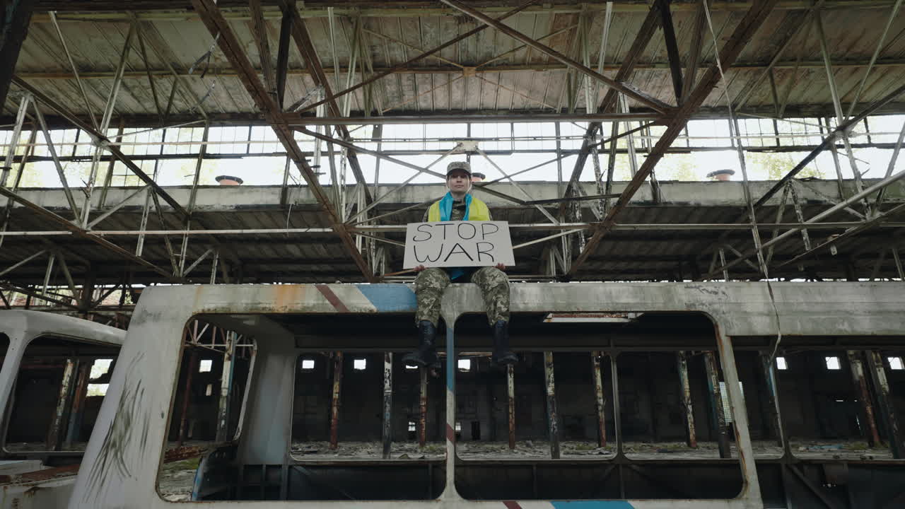 Protester Sits on War Damaged Structure, Holding a Sign