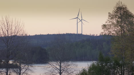 golden hour - wind turbines spin over a forest and lake in sweden