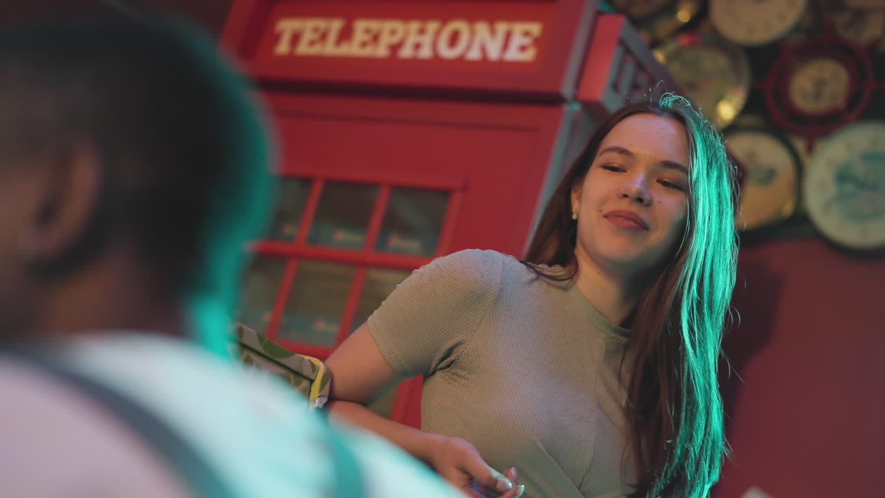 женщина, впечатленная подругой, играющей на пианино в клубе. веселая брюнетка слушает выступление музыканта в ночном клубе. длинноволосая женщина сидит рядом с пианистом