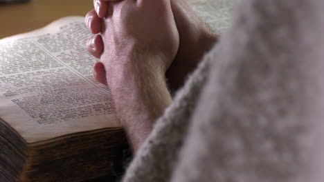 hands of a caucasian friar praying over a bible