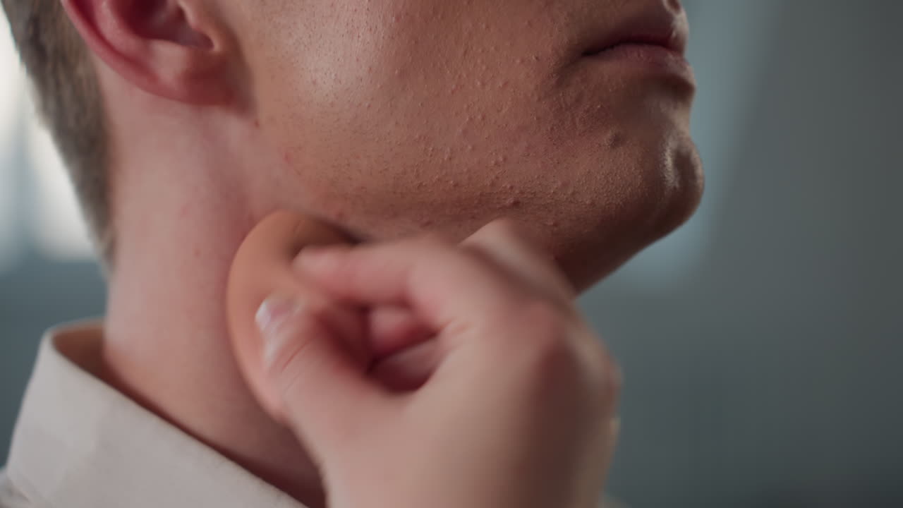 close up of makeup sponge blending foundation on male jawline highlighting grooming routine with soft blurred background showcasing smooth application technique and natural skin texture