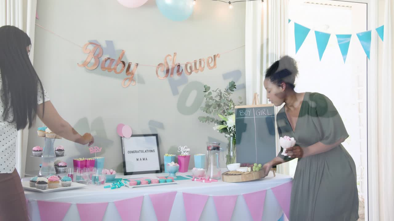 Dos mujeres entran en la cocina con bandejas y preparan la mesa para un baby shower; hay números superpuestos.