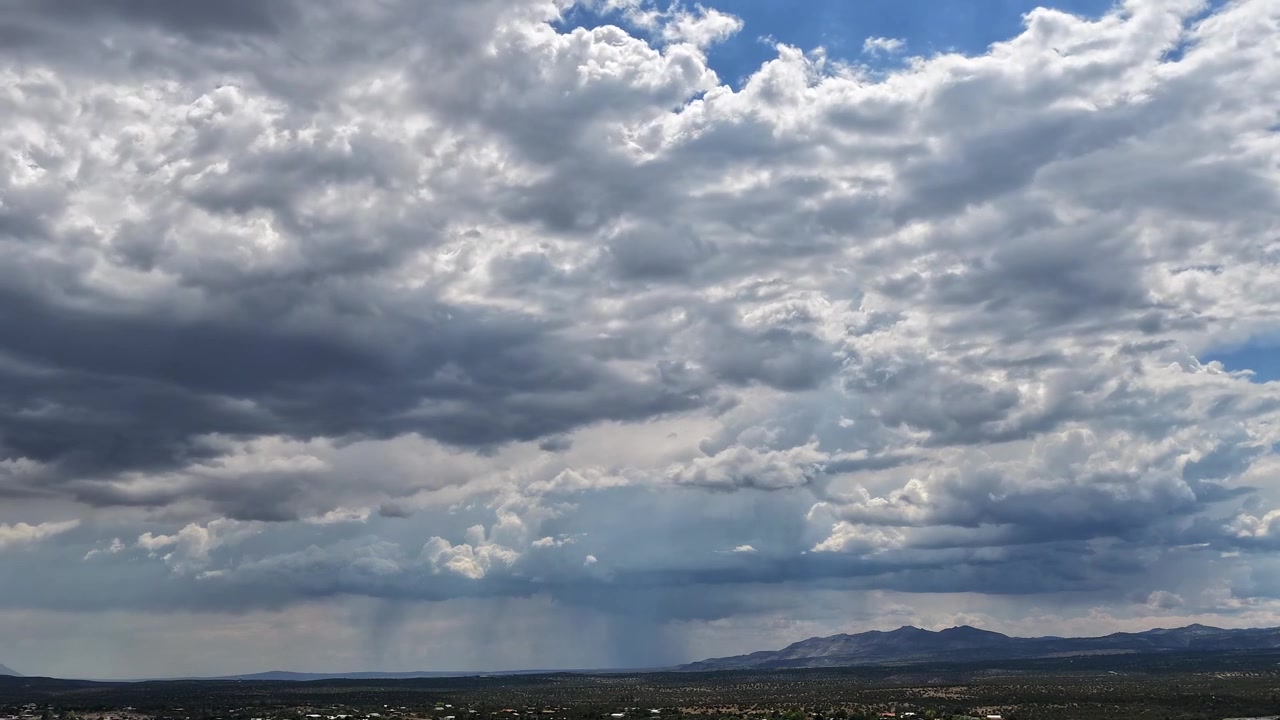 Timelapse 4K con drone che cattura una fitta coltre di nuvole grigie che si muovono rapidamente sopra la testa. Deboli scrosci di pioggia e precipitazioni sparse si spostano attraverso l'ampio e piatto orizzonte sopra una catena montuosa distante