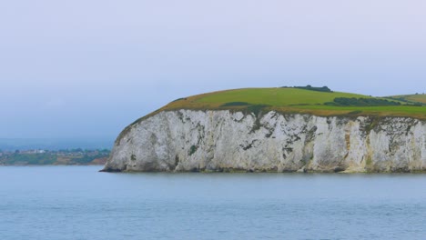 white chalk cliffs along english coastline with fields on top and small village in distance near poole uk 4k