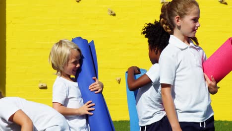 school kids holding yoga mat and interacting with each other