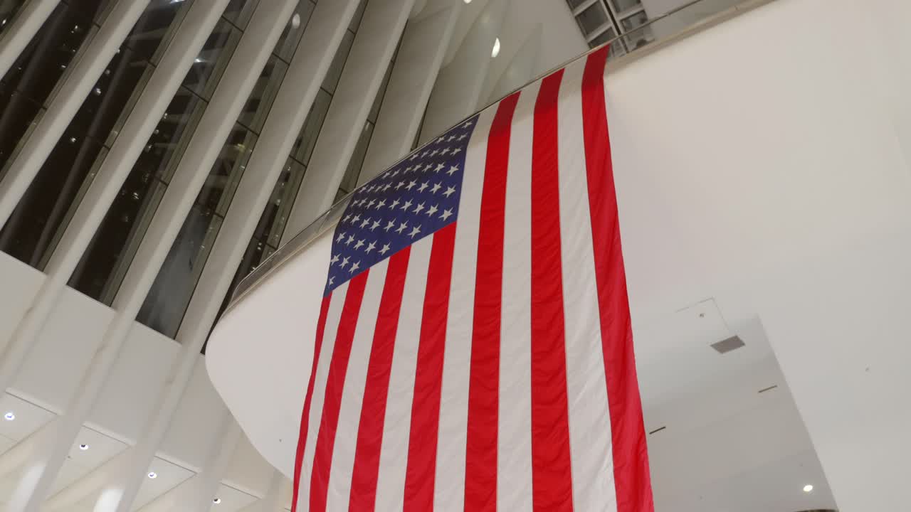 The American flag billows gracefully in a contemporary New York City building. Bright, open spaces frame the vibrant red, white, and blue colors of the flag, evoking a sense of patriotism