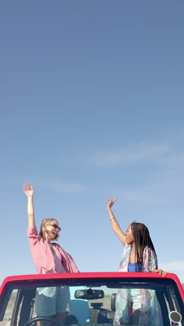 vertical video: women enjoying road trip, standing in car with arms raised, smiling