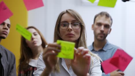 mujer de negocios confundida en una reunión de equipo pega la nota de color en la pared de vidrio