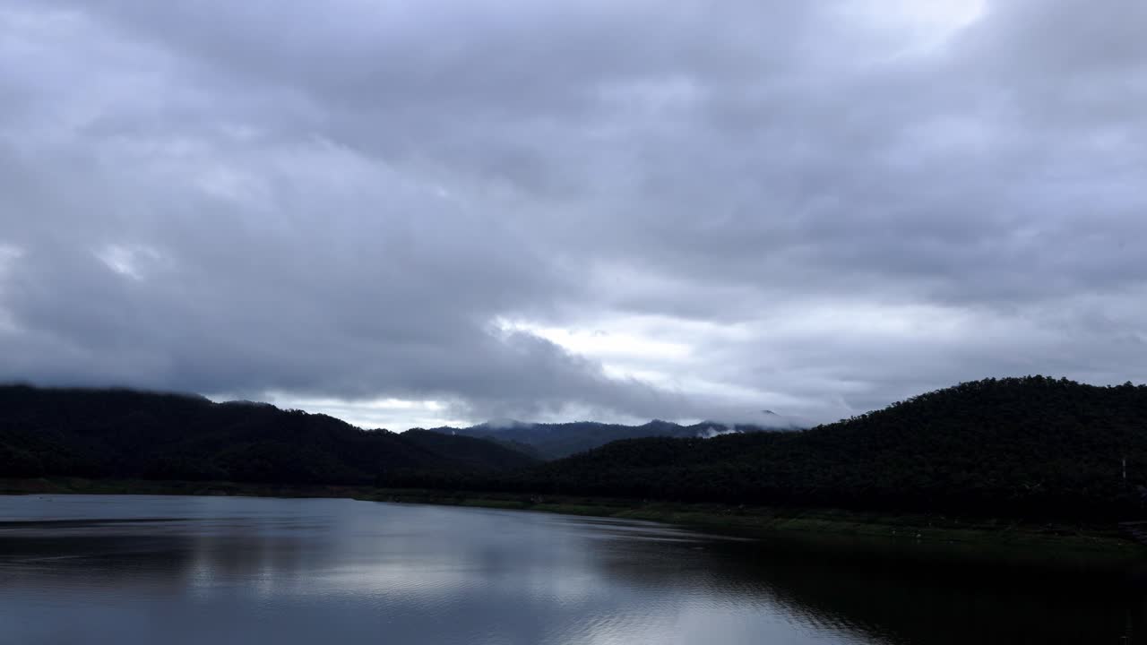 일출의 광선으로 아침에 산 범위와 호수에 뇌우 후 흐린 하늘의 시간 경과