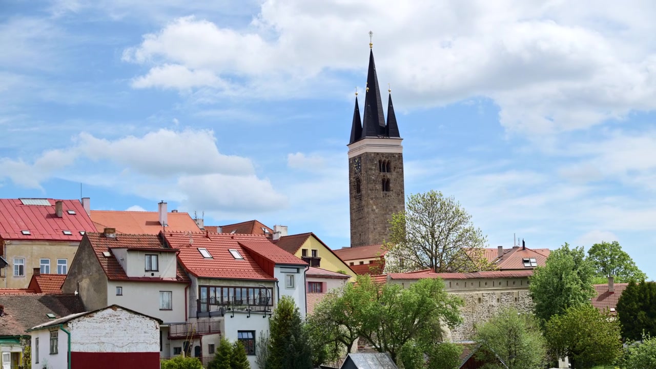 Una torre campanaria in pietra con una guglia scura sopra i tetti rossi di un centro storico, Telč, Repubblica Ceca