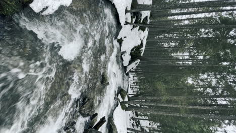 Flujo-De-Agua-Y-Roca-Rápida-En-El-Bosque-De-Invierno-Con-Orientación-Vertical-De-Nieve