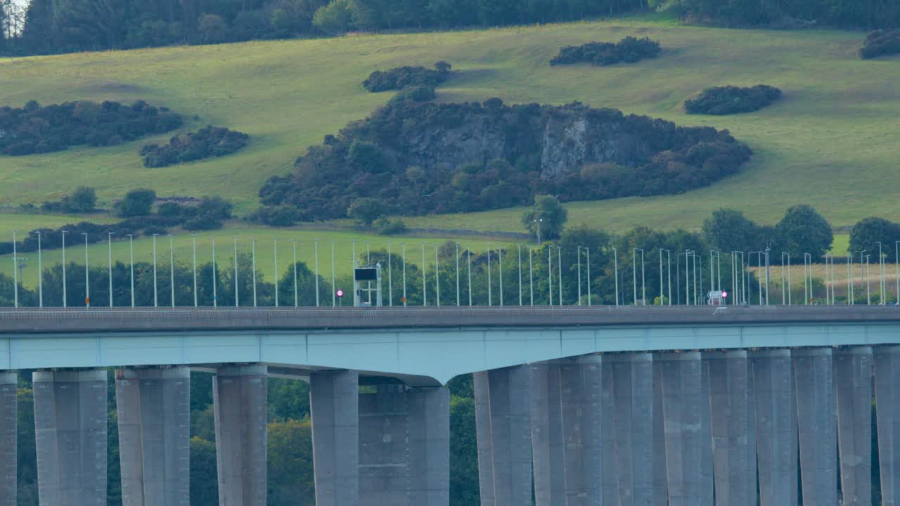 A truck drives across Tay Road Bridge, scenic hills in background, steady camera, natural daylight