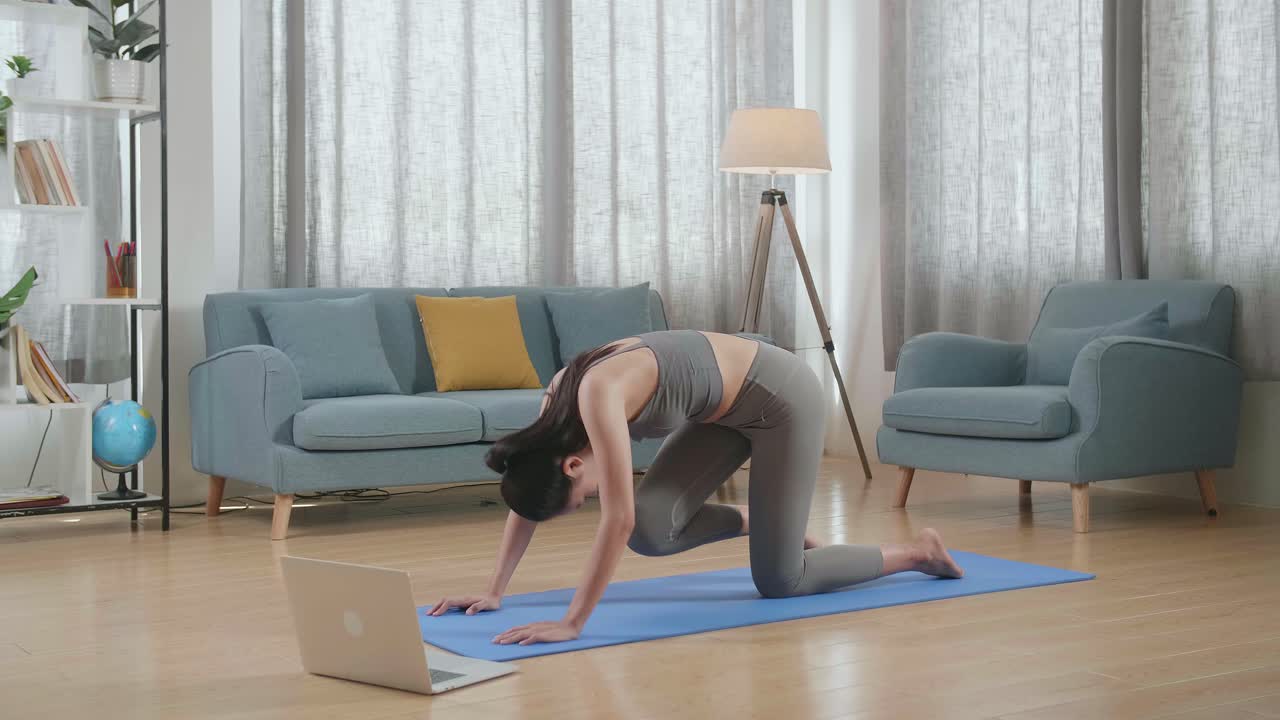 젊은 아시아 운동선수 여성이 노트북 컴퓨터를 통해 온라인 코치와 함께 집에서 운동, 스트레칭 및 요가를 연습하고 있습니다.
