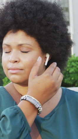 mujer biracial feliz de talla plus que usa un teléfono inteligente y lleva auriculares en la ciudad