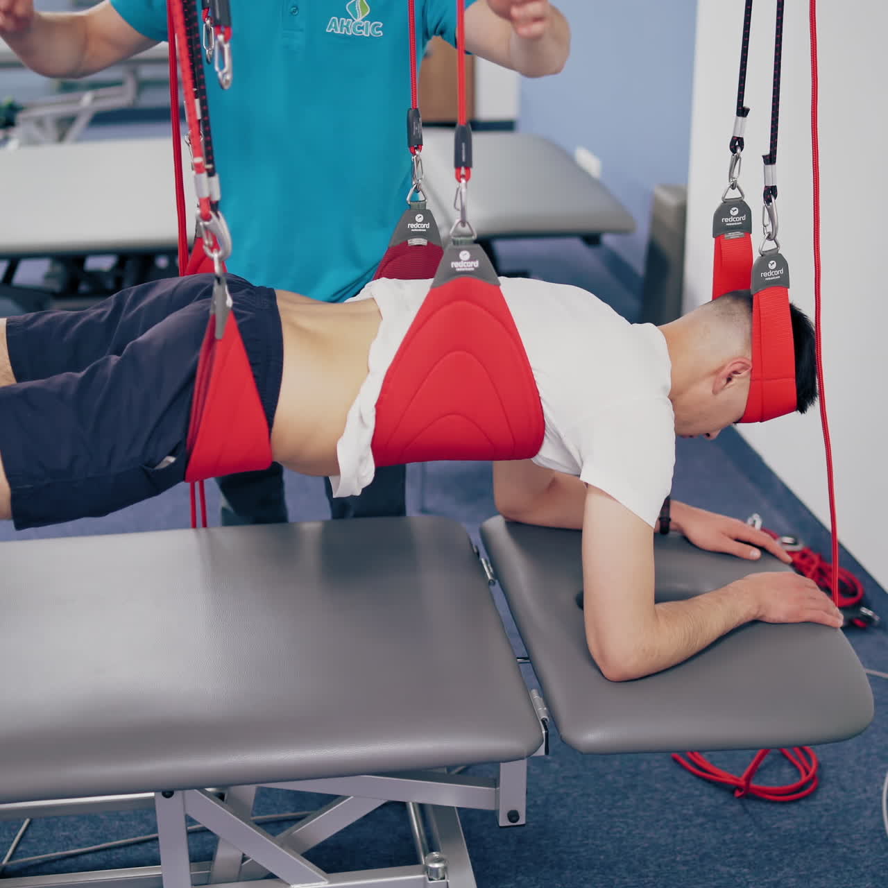 Man's body is hanging on the special suspension ropes on the modern rehab center background. Personal trainer helps the man to do the exercises with the new equipment to recover.