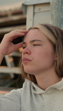 primer plano de una joven que descansa con la cabeza en la mano, su expresión refleja una profunda contemplación, la cálida luz del sol en el fondo crea un suave resplandor