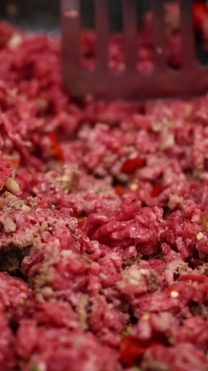 Primo piano di carne macinata cotta con una spatola in una padella. Una luce brillante evidenzia la consistenza e il colore.