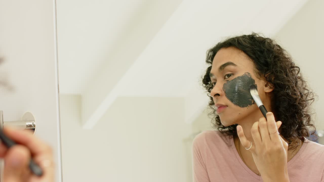 At bathroom mirror nonbinary adult applying charcoal mask with brush for even coverage copy space