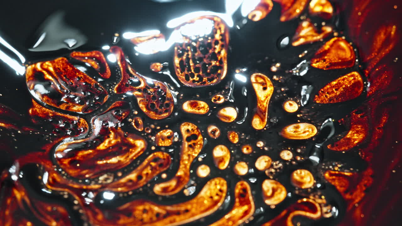 Molten black and orange liquid textures blend and form intricate patterns in a mesmerizing macro shot